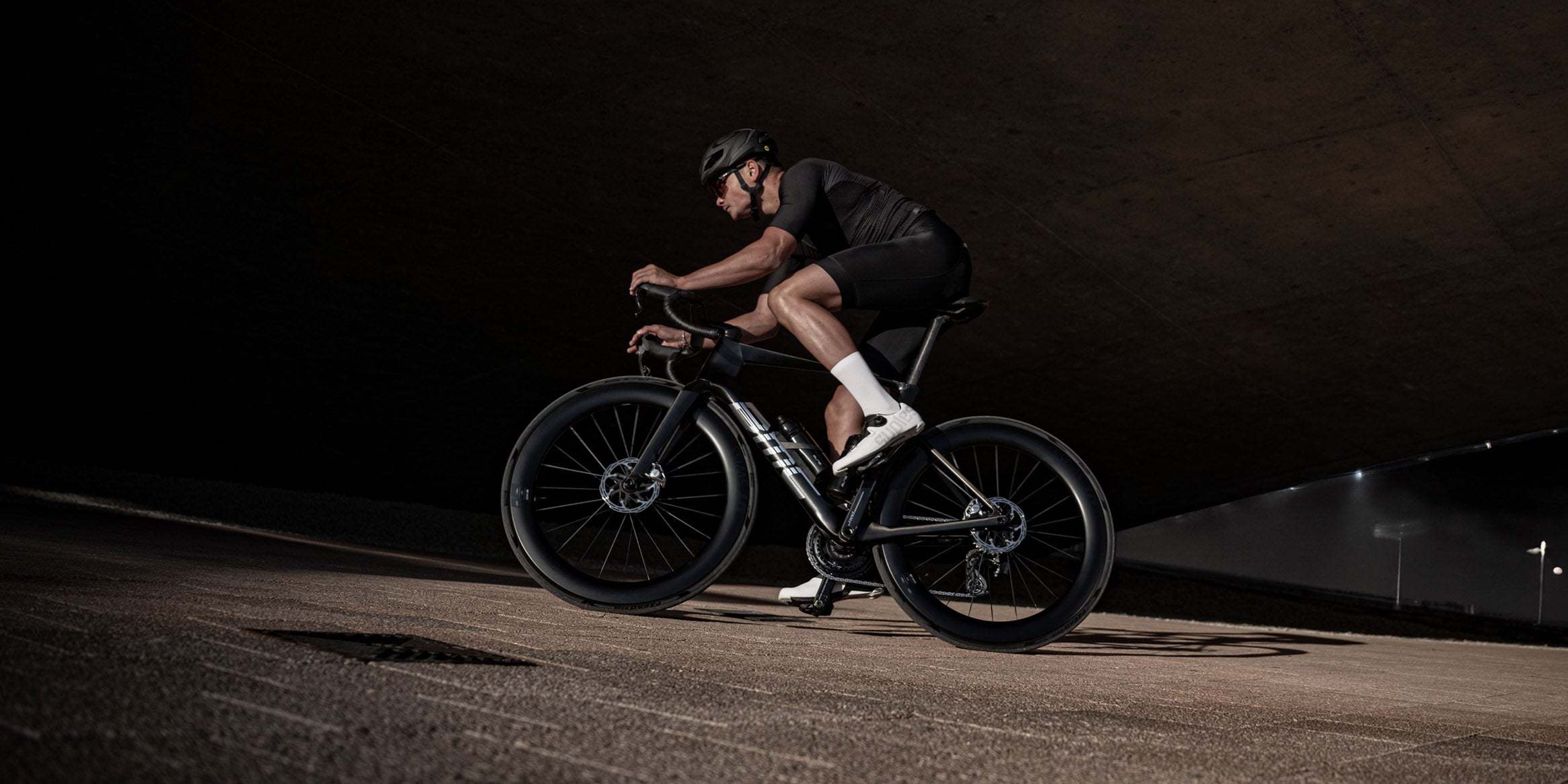 Racer riding a lightweight Mpc series carbon road bike under a concrete arch 